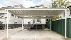 Een overdekt buitengebied met een trap die naar een gebouw leidt, een groen hek en een waarschuwingsbord.