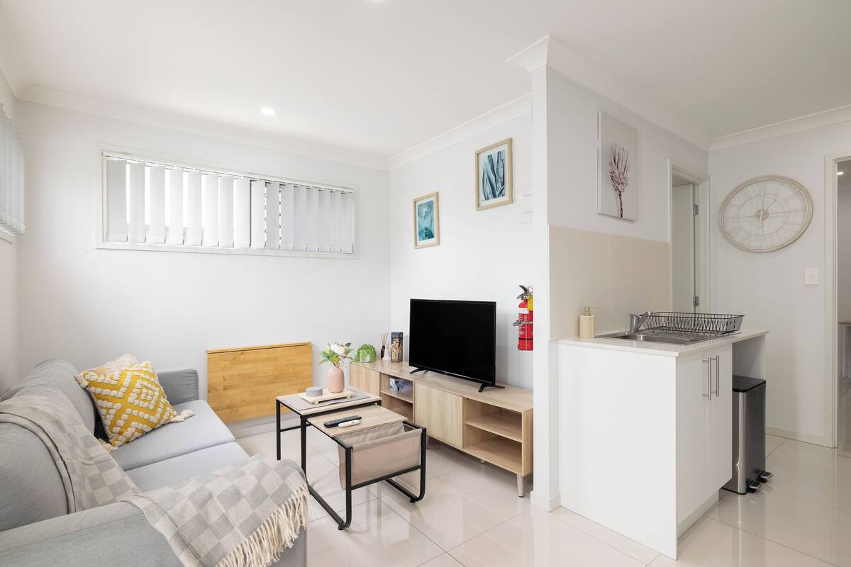 A modern living room with a sofa, TV, and a small kitchen area.