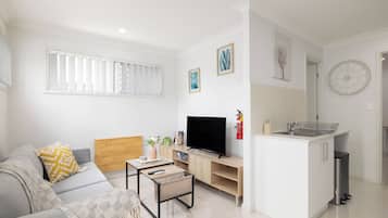 A modern living room with a sofa, TV, and a small kitchen area.