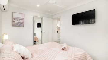 A bedroom with a bed, a ceiling fan, a TV, and a door leading to a bathroom.