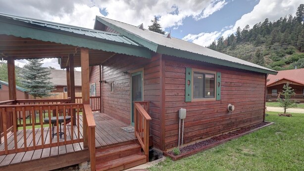 A wooden cabin with a porch, a small front yard, and a mountainous backdrop.