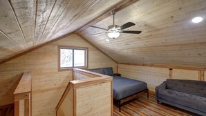 A loft bedroom with a sloped ceiling, a ceiling fan, a bed, a couch, and a window.