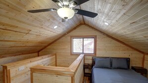 A cozy attic bedroom with a sloped ceiling, a single bed, a window, and a ceiling fan.
