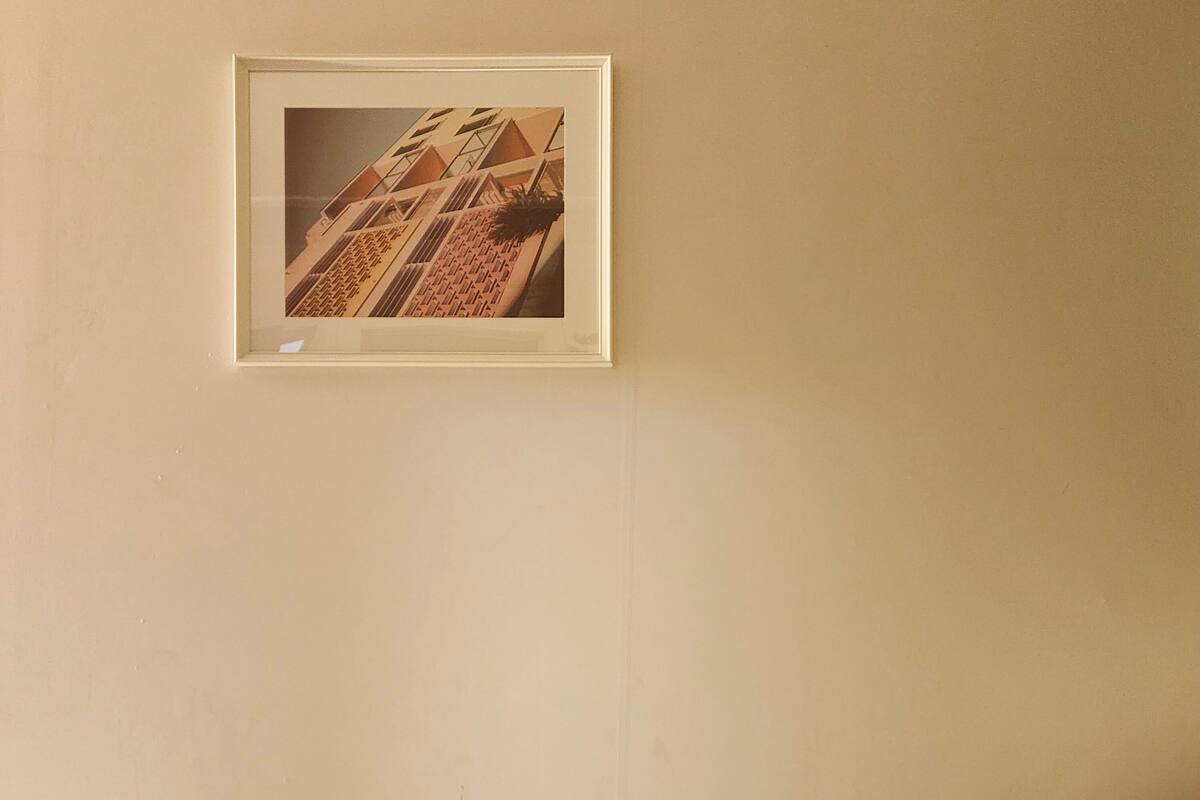 A bed with a white sheet and a framed picture of a building on the wall.