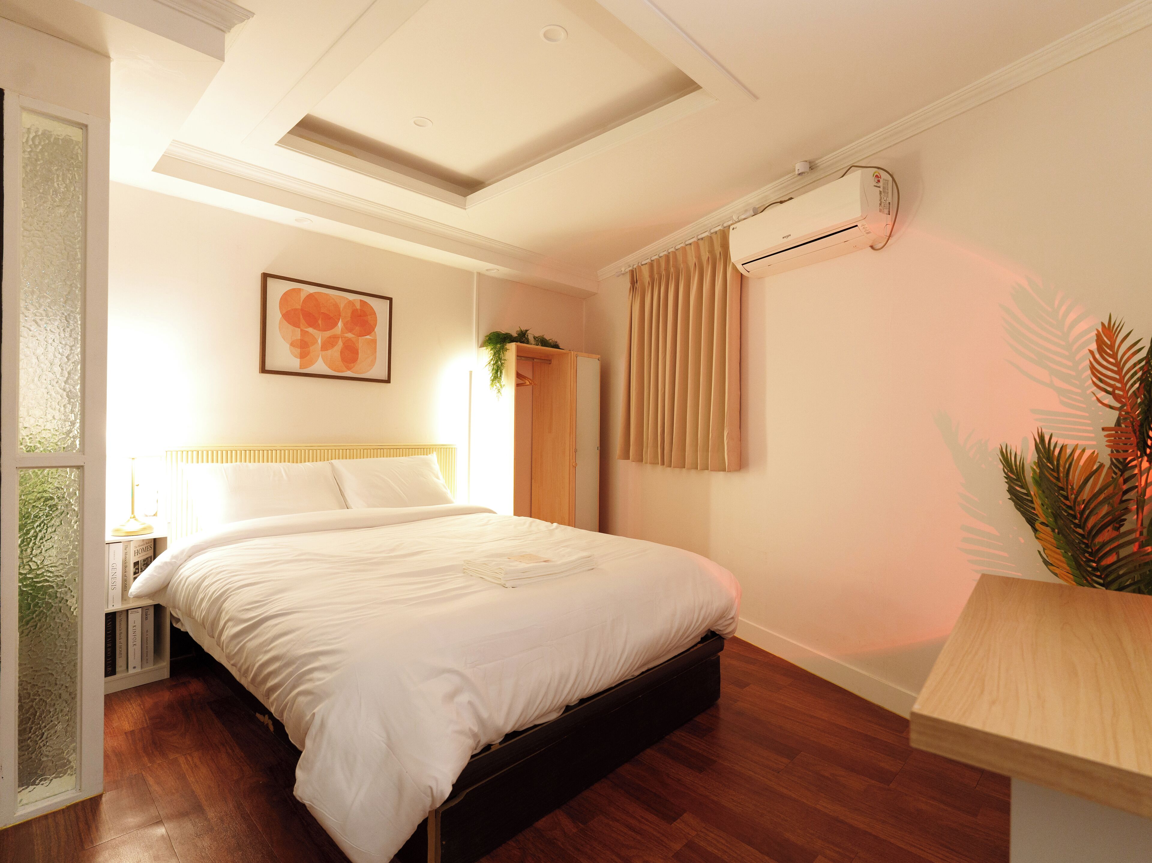 A neatly arranged bedroom with a bed, a bedside table, a hanging plant, and a window with curtains.
