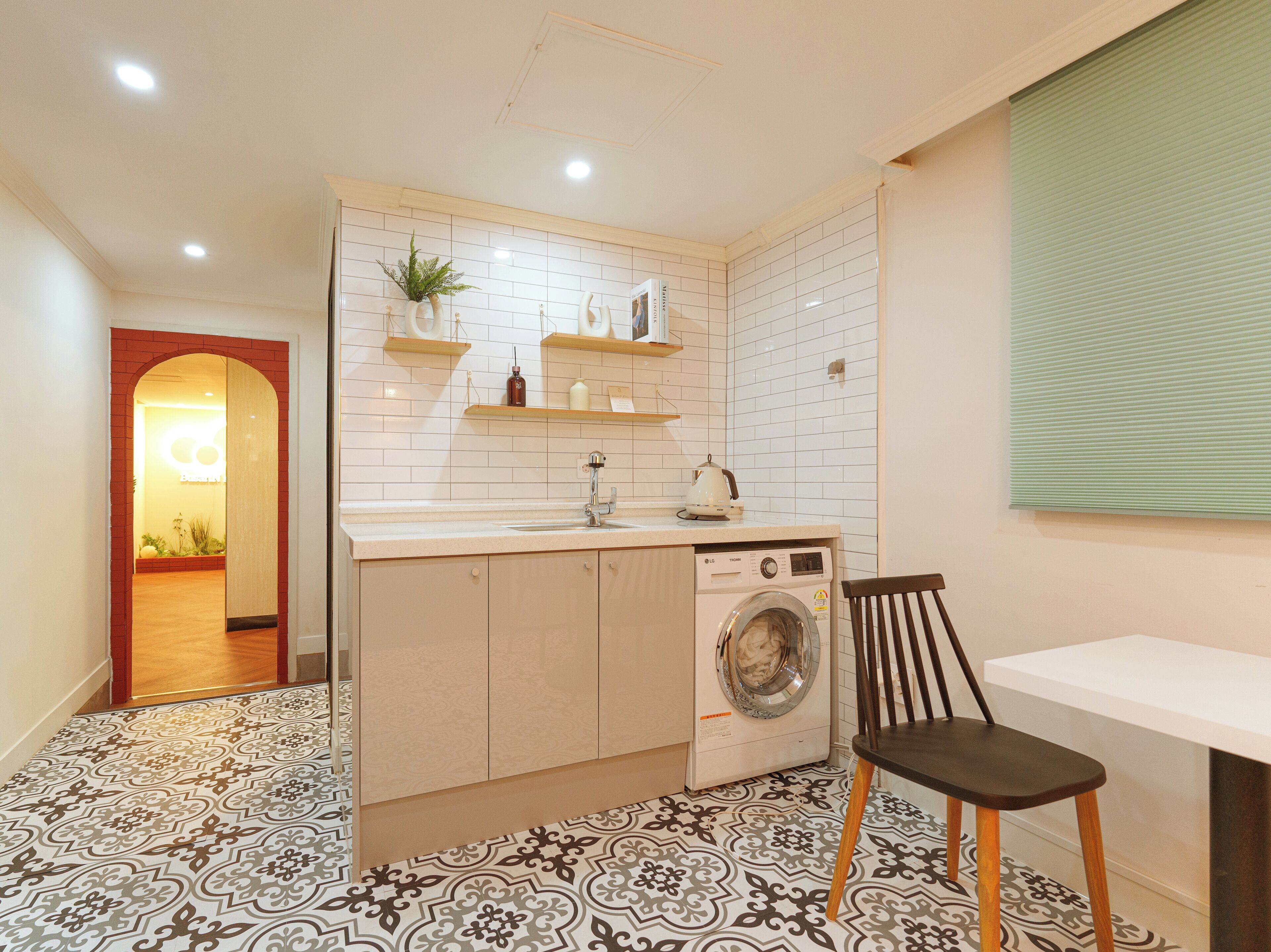 A compact kitchen with a washing machine, a sink, and a chair.