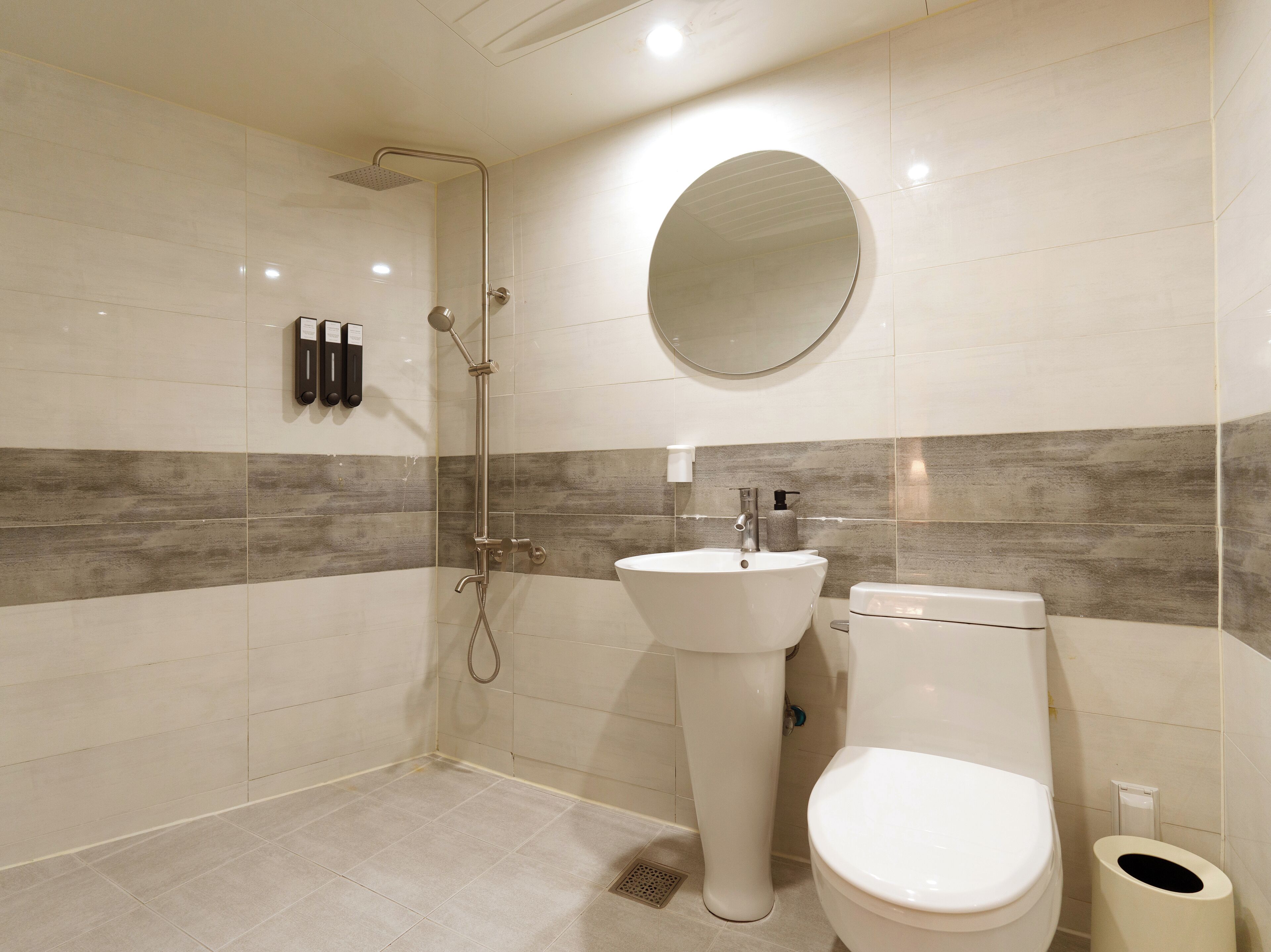 A modern bathroom with a shower, sink, toilet, and a round mirror.