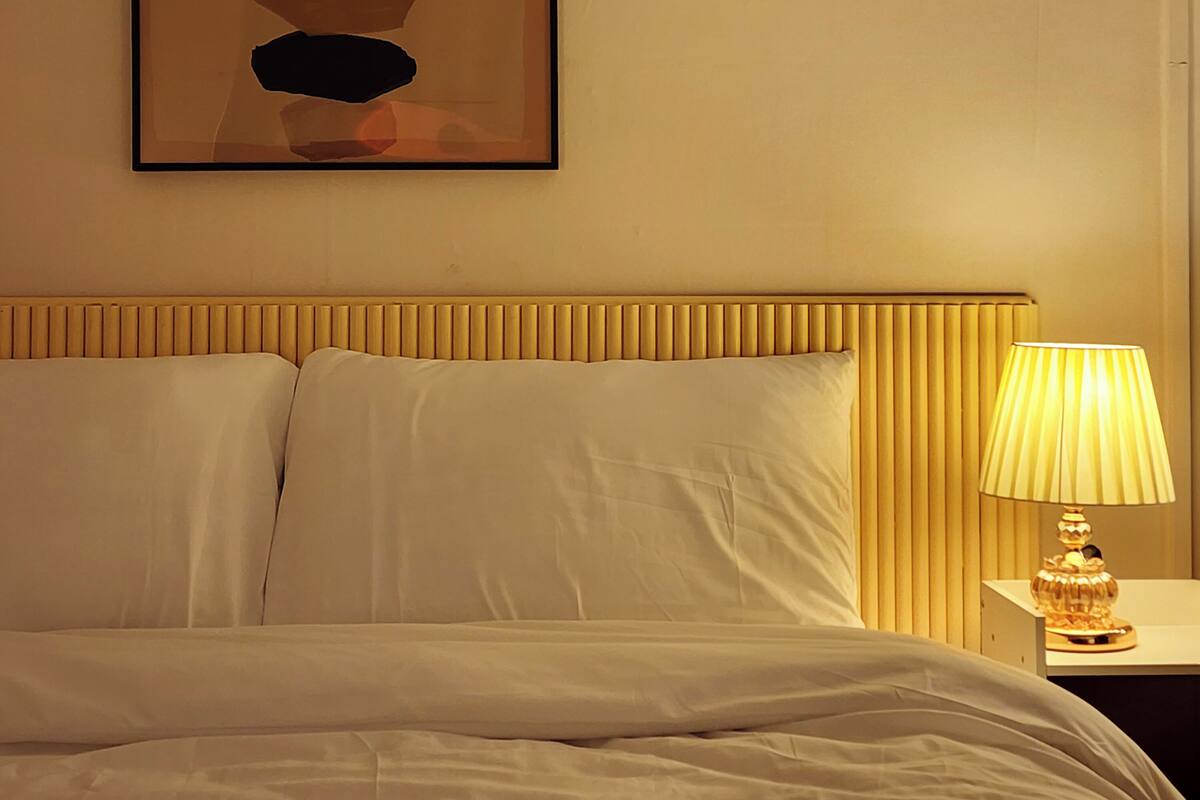 A hotel room with a bed, a bedside lamp, and a wall-mounted abstract art piece.