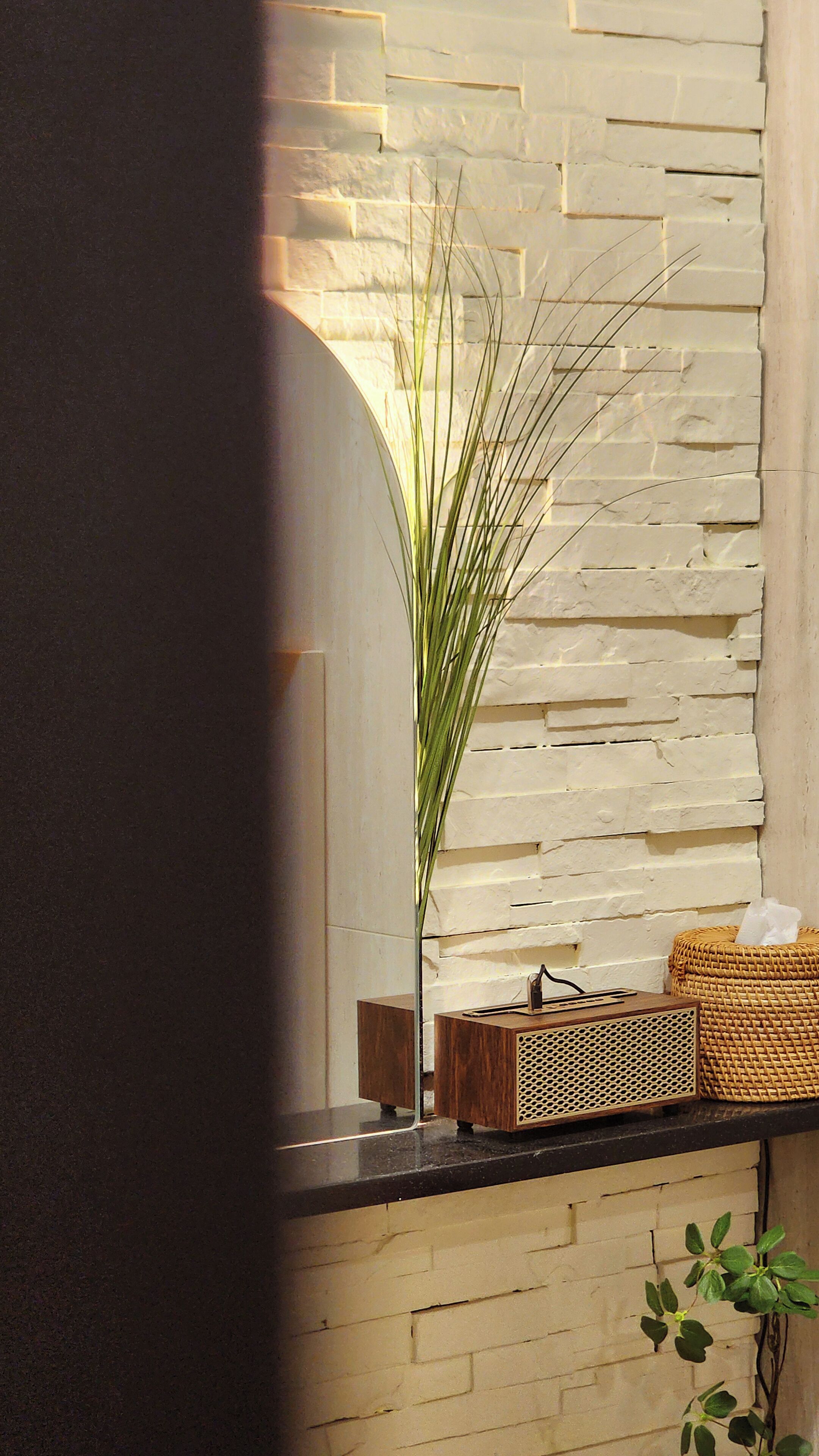 Een modern interieur met een witte bakstenen muur, een houten bankje en een kleine tafel met een radio en een rieten mand.