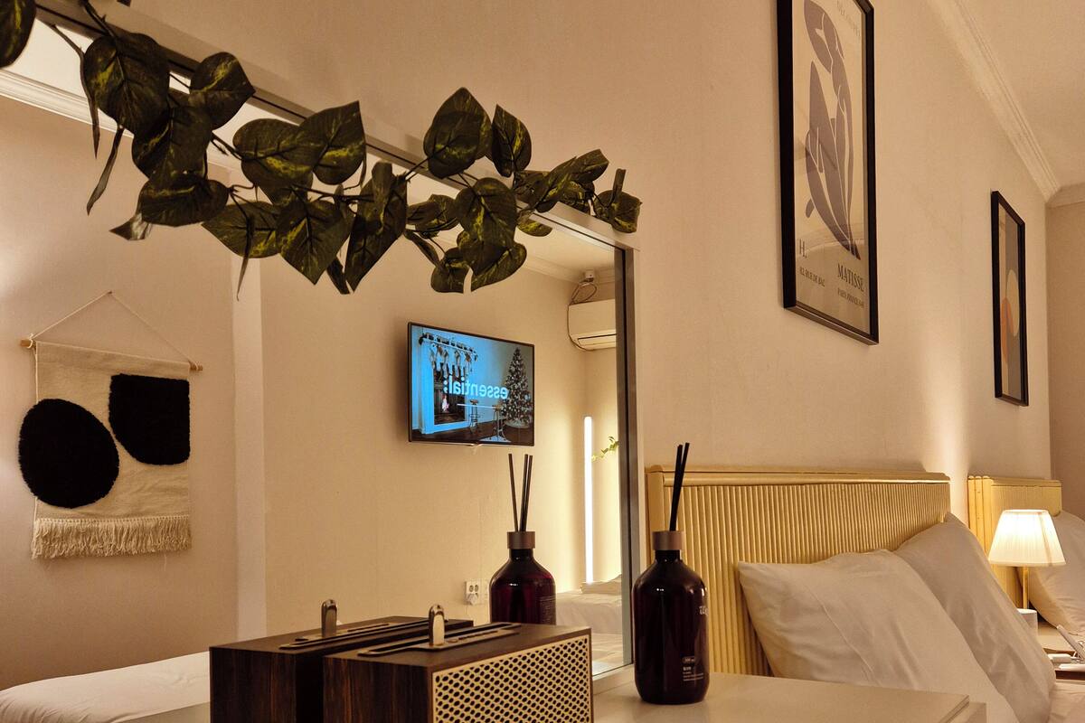 A hotel room with a bed, a bedside table with a bottle, a TV, and a wall-mounted mirror.