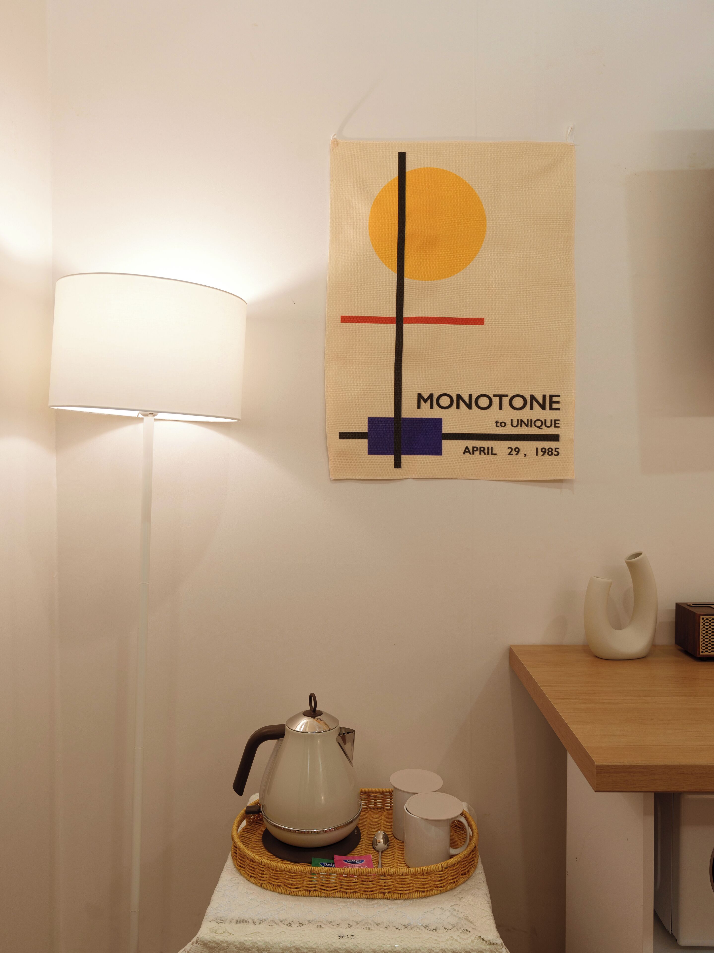 Una habitación con una lámpara de pared, un cartel con texto, una mesa con tetera, tazas y una bandeja.