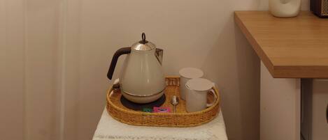 Una habitación con una lámpara de pared, un cartel con texto, una mesa con tetera, tazas y una bandeja.