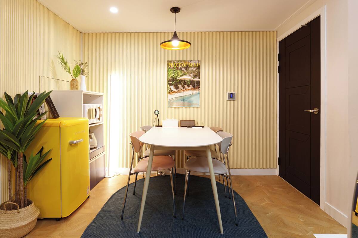 A dining area with a round table, chairs, a yellow refrigerator, and a potted plant.