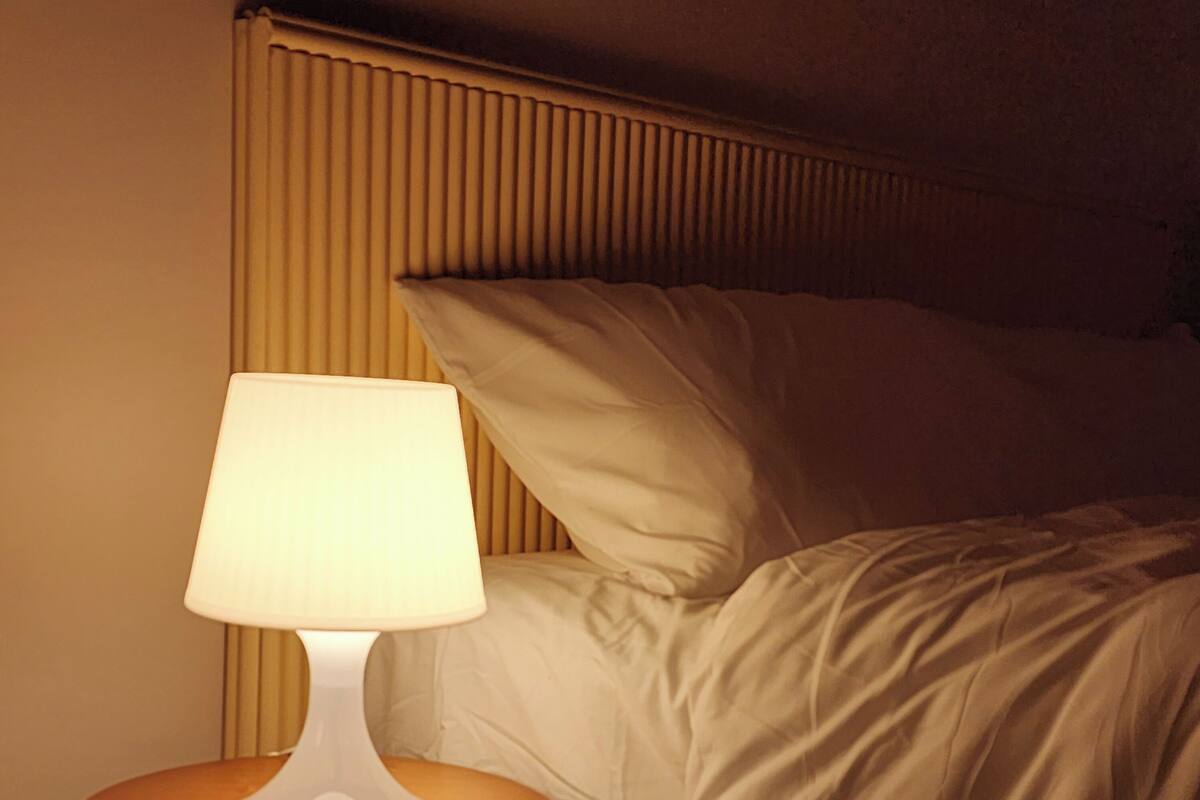 A bed with white bedding, a round bedside table with a white lamp, and a wooden headboard.