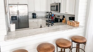 Una cocina moderna con armarios blancos, electrodomésticos de acero inoxidable, encimera de mármol y tres taburetes.