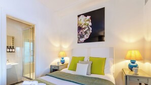 Ett hotellrum med en säng, två sängbord med lampor, en spegel, ett badrum med handfat och ett stort konstverk med blommotiv på väggen.