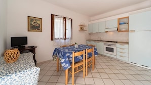 A compact room with a dining table, chairs, a television, a kitchen area with cabinets, and a window with curtains. - La Conchiglia Apartment (Seccheto)