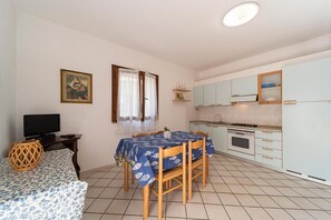 A compact room with a dining table, chairs, a television, a kitchen area with cabinets, and a window with curtains.