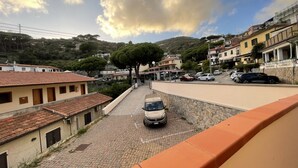 A paved street with a parked car, buildings with red-tiled roofs, and a hill with trees in the background. - La Conchiglia Apartment (Seccheto)