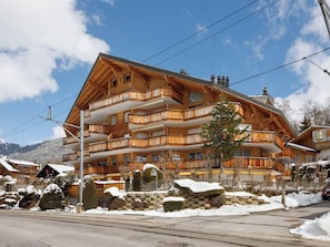 A multi-story wooden building with balconies, a stone wall, and snow-covered surroundings.