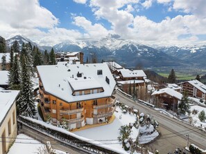 A mountain lodge with multiple balconies, a snow-covered roof, and a view of snow-capped mountains.