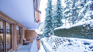 Un edificio de madera con ventanas grandes y una banca en el exterior. Se ven árboles cubiertos de nieve y un seto al fondo.