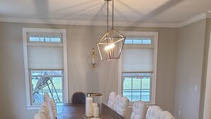 Une salle à manger spacieuse avec une longue table en bois, des chaises rembourrées et un luminaire suspendu moderne.