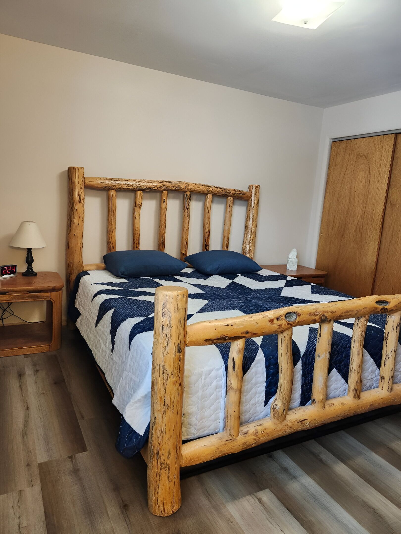 A wooden bed with a quilt, a nightstand, a lamp, and a wardrobe.