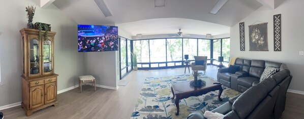 Un salón amplio con una televisión grande, un aparador de madera, un sofá y vistas por grandes ventanales.
