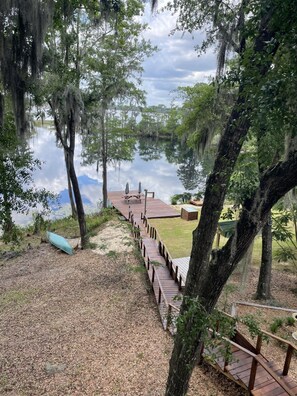 A wooden deck leading to a dock over a calm lake, surrounded by trees and a grassy area. - 4-bedroom Lake House 45 Minutes from the Beach! (Chipley)