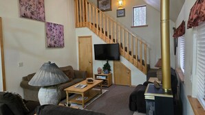 A living room with a sofa, coffee table, lamp, fireplace, television, and a staircase. - Northwoods (#12) Cabin in the Pines (Pinetop-Lakeside)