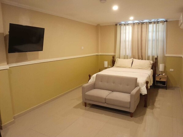 A bedroom with a bed, a television mounted on the wall, a nightstand, and a sofa. - Cozy 1-bedroom apartment with AC, WiFi kitchen in the Capital City, Georgetown (Georgetown)
