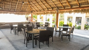 An outdoor patio area with thatched roof, wicker furniture, and a view of a building in the background. - Tropical Getaway in Flamingos near Beach (Bucerías)