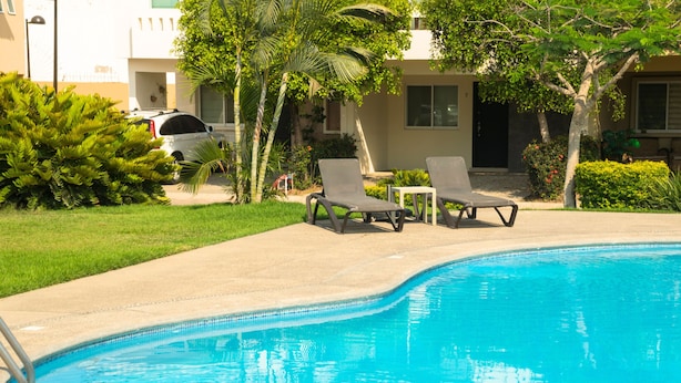 A swimming pool with lounge chairs, a parked car, and a building in the background. - Tropical Getaway in Flamingos near Beach (Bucerías)