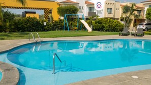 A swimming pool with a blue slide, surrounded by greenery and a building with a yellow facade. - Tropical Getaway in Flamingos near Beach (Bucerías)