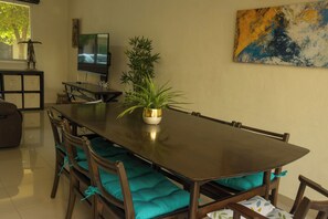 A dining area with a long table, chairs with teal cushions, a potted plant, a television, and a painting on the wall. - Tropical Getaway in Flamingos near Beach (Bucerías)