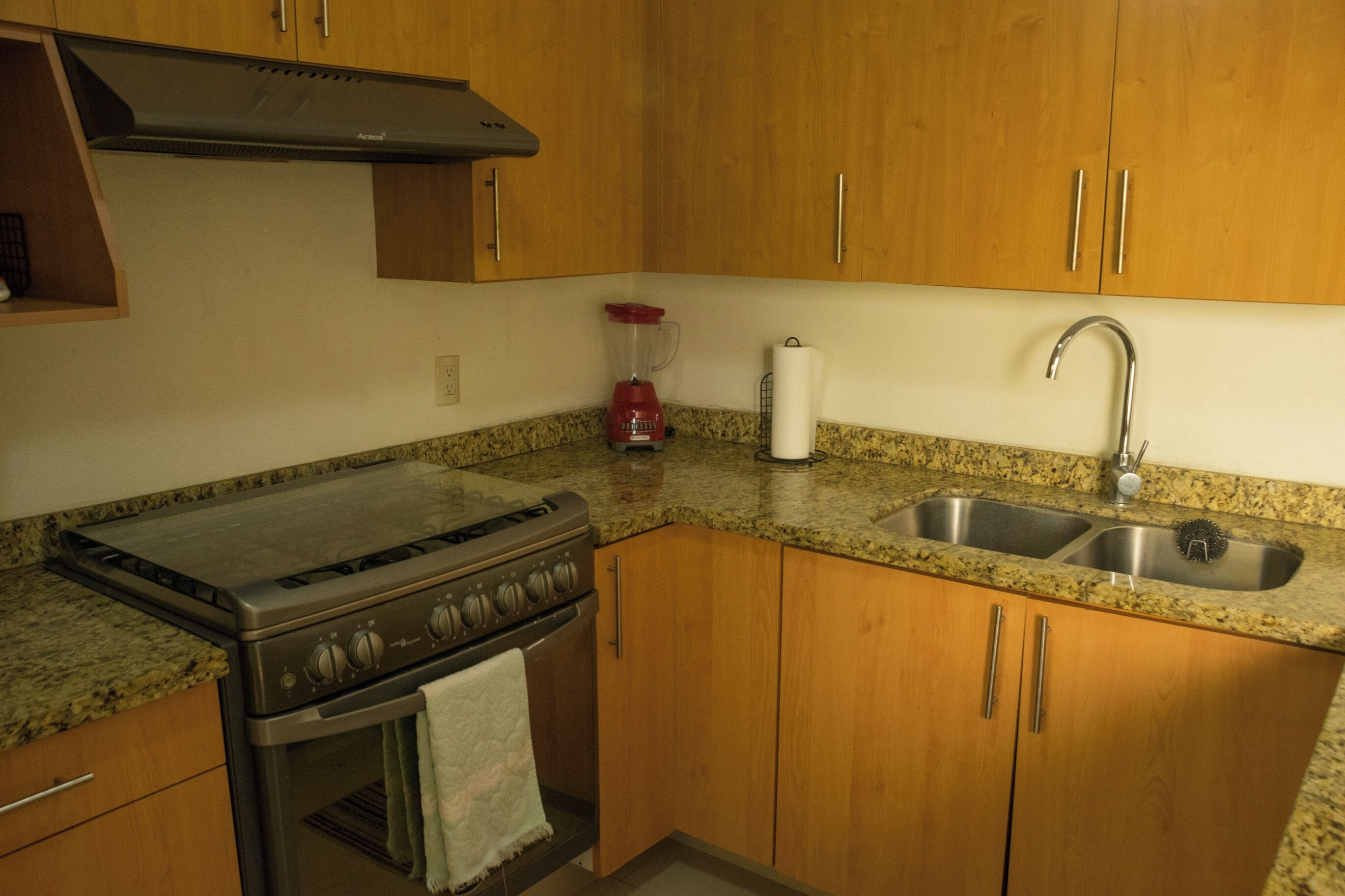 A kitchen with wooden cabinets, a stainless steel stove, a sink, and a red blender.