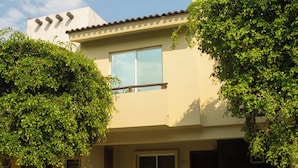A two-story house with a balcony, a front door, and a small front yard with grass and a tree. - Tropical Getaway in Flamingos near Beach (Bucerías)