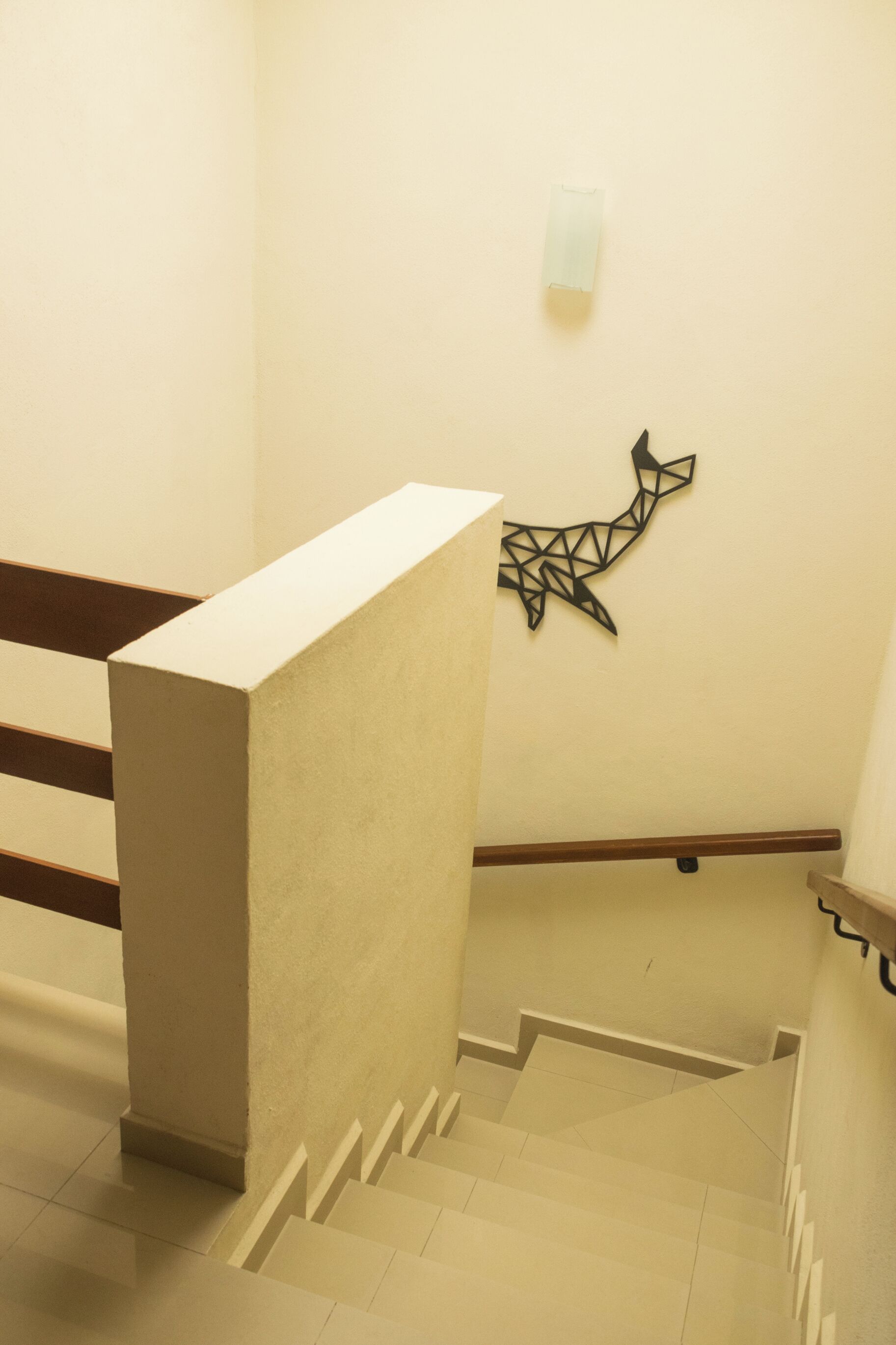 A staircase with a handrail, a wall-mounted light fixture, and a geometric wall art piece.