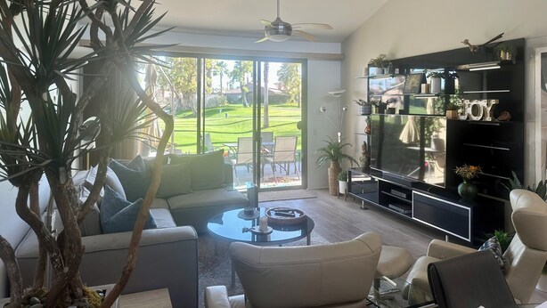 A modern living room with a sofa, coffee table, and a large TV. There is a plant and a ceiling fan. - Your Palm Desert Vacation Getaway at the Palm Valley Country Club is calling! (Palm Desert)