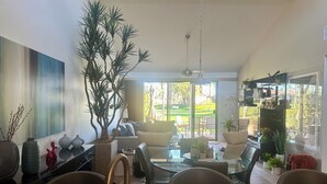 A modern living room with a large plant, a dining area with a glass table, and a kitchen with a granite countertop. - Your Palm Desert Vacation Getaway at the Palm Valley Country Club is calling! (Palm Desert)