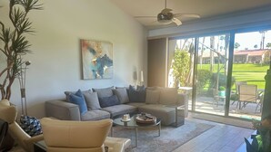 A modern living room with a sectional sofa, a coffee table, and a large window offering a view of a garden. - Your Palm Desert Vacation Getaway at the Palm Valley Country Club is calling! (Palm Desert)