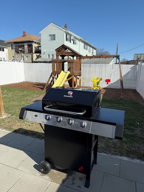 A charcoal grill with four burners, a side table, and a swing set in a backyard. - Beautiful 3BR+Office+Parking+Backyard near Boston-Cambridge. (Medford)