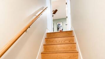 A wooden staircase with a handrail, leading to a room with a ceiling fan and a fire extinguisher mounted on the wall.