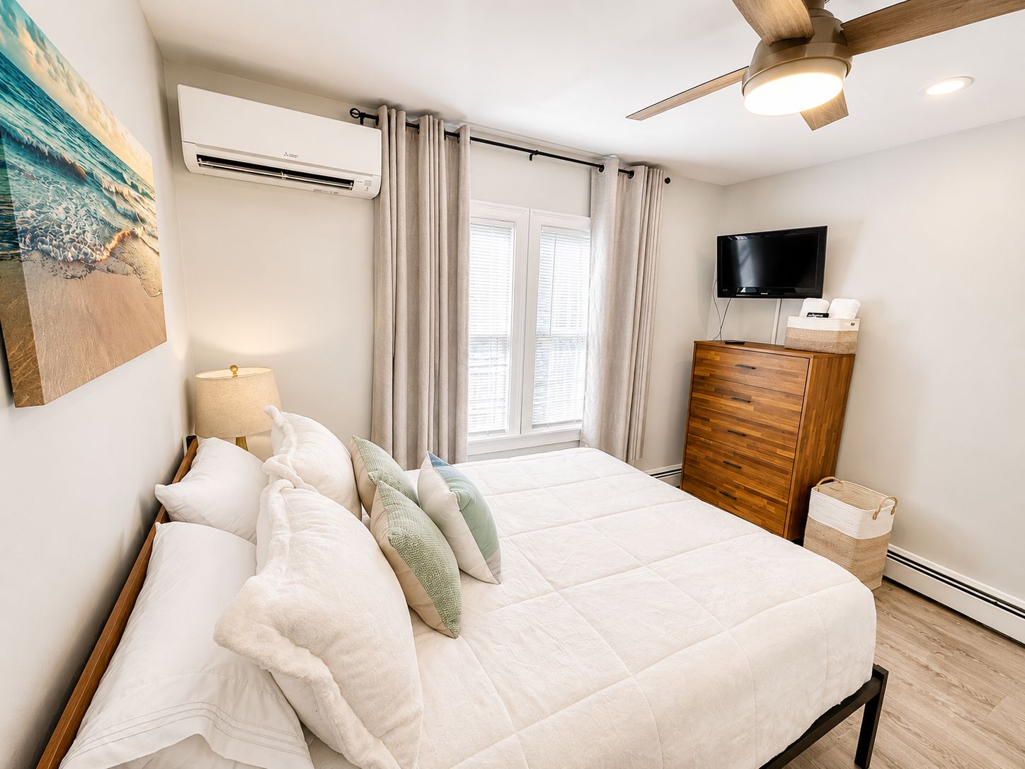 A bedroom with a bed, an air conditioner, a TV, a wooden dresser, and a window with curtains.