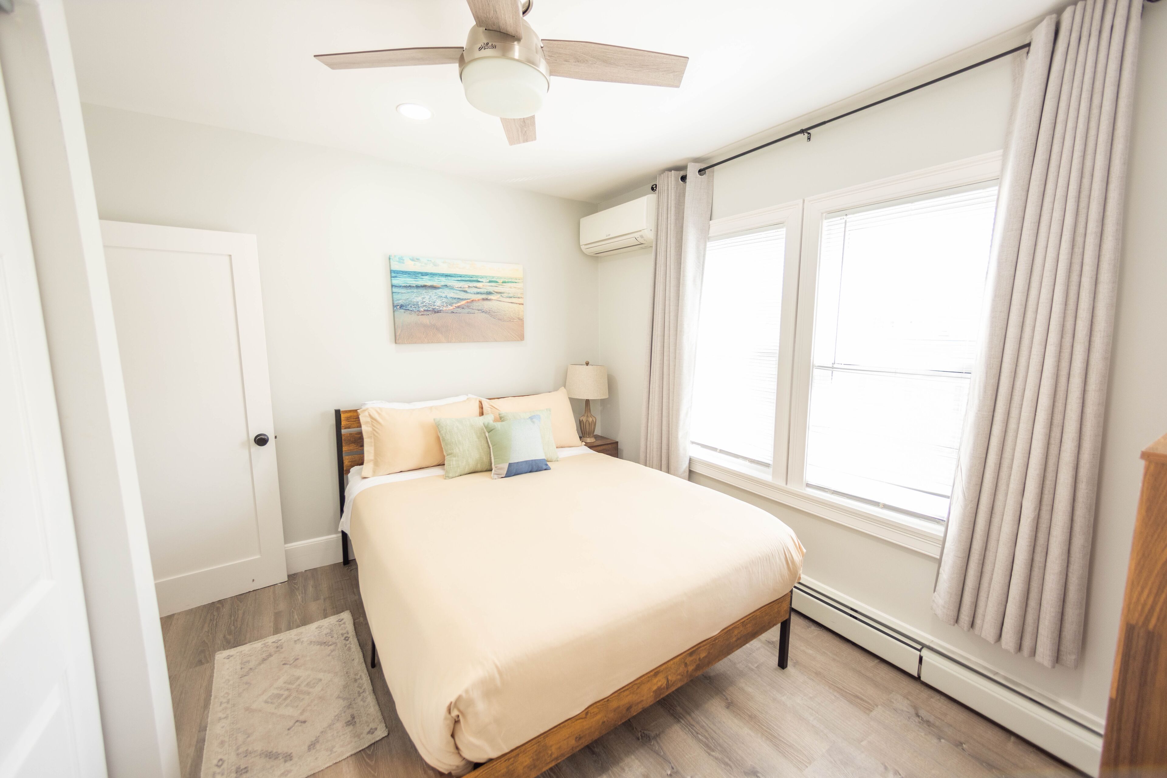 A bedroom with a bed, a ceiling fan, a painting on the wall, and a window with curtains.