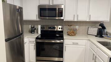 A modern kitchen with stainless steel appliances, white cabinetry, and a hexagonal tile backsplash.