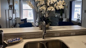 A modern kitchen with a white countertop, stainless steel sink, and a vase with white orchids.