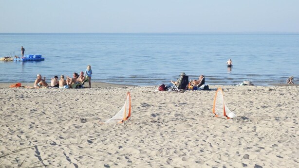 Une plage de sable où des gens se détendent et où certains se baignent.