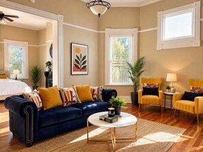 A room with a blue sofa, yellow armchairs, a white coffee table, and a large window with blinds.